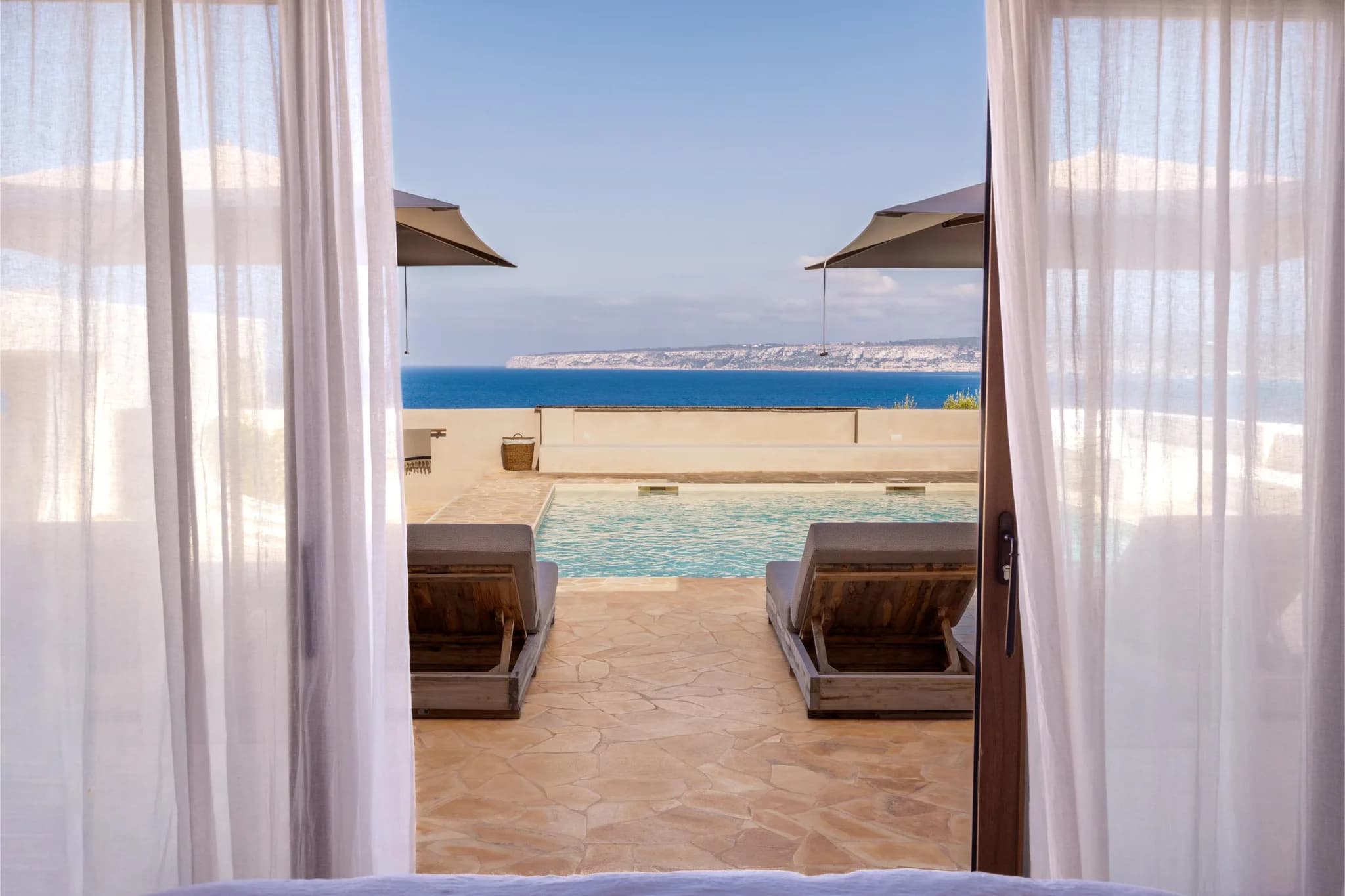 Pool and coastline seen through linen curtains
